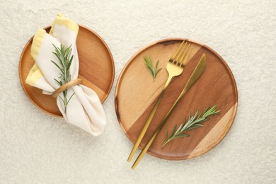 Photo of Stylish setting with cutlery, napkin, rosemary and plates on light textured table, flat lay