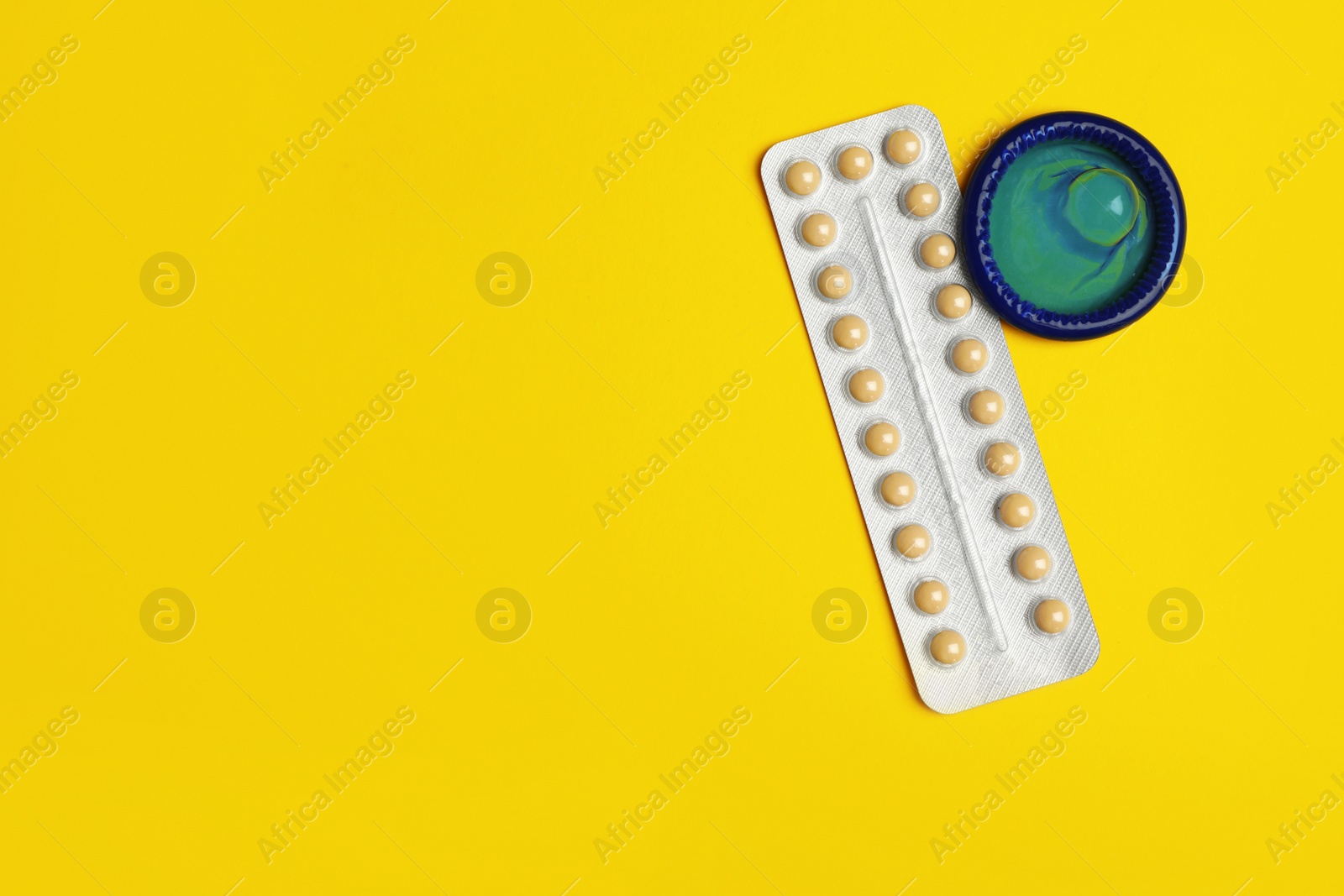 Photo of Condom and birth control pills on yellow background, flat lay with space for text. Safe sex concept