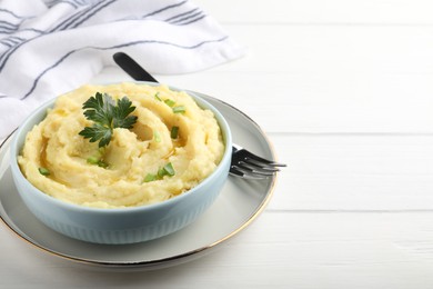 Photo of Bowl of tasty mashed potatoes with parsley and green onion served on white wooden table. Space for text