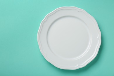 Photo of Empty white ceramic plate on turquoise background, top view. Space for text