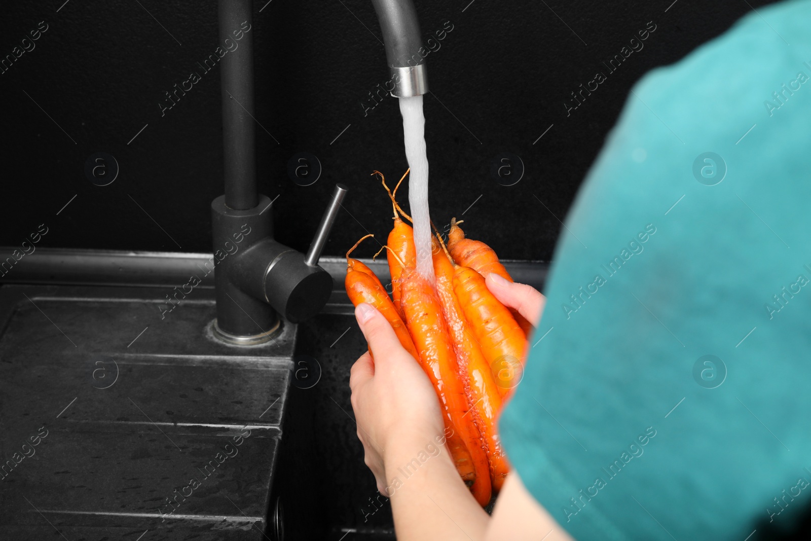 Photo of Woman washing fresh ripe juicy carrots under tap water in sink, closeup