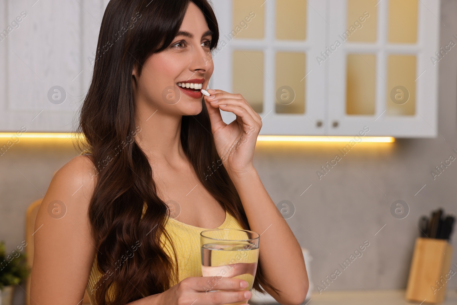 Photo of Beautiful woman taking vitamin pill in kitchen