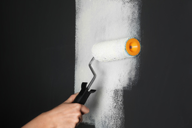 Photo of Woman painting grey wall with white dye, closeup