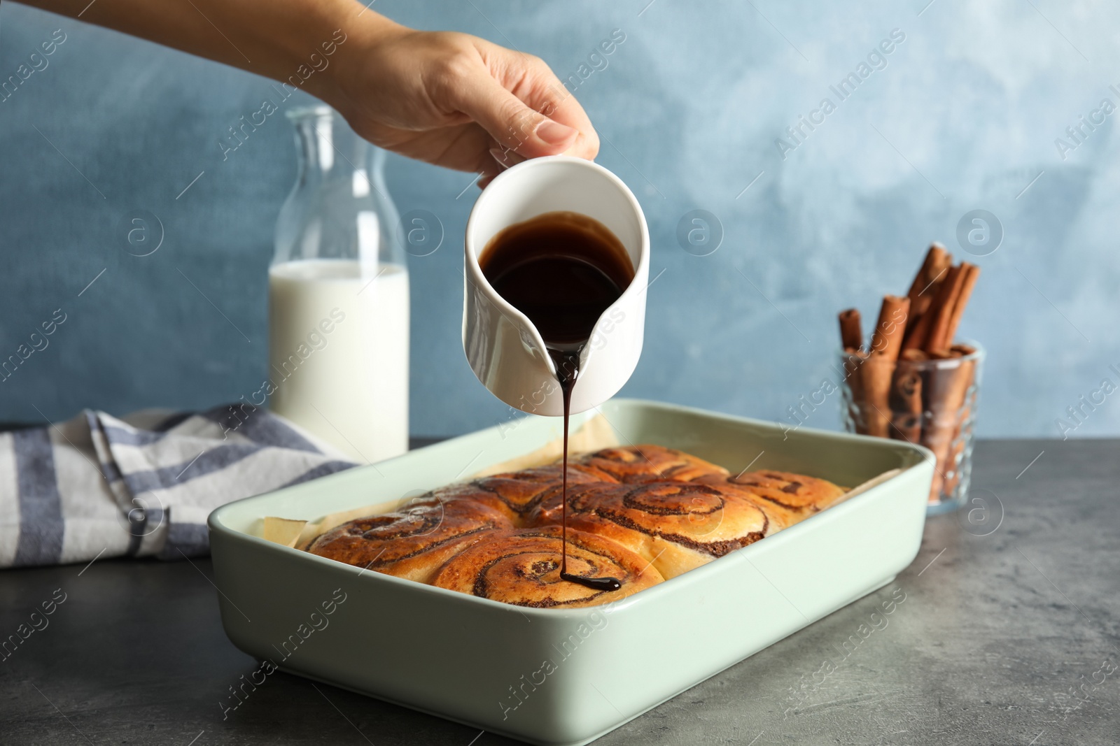 Photo of Woman pouring chocolate syrup onto freshly baked cinnamon rolls on table, closeup
