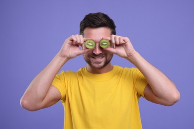Photo of Man covering his eyes with halves of kiwi on purple background