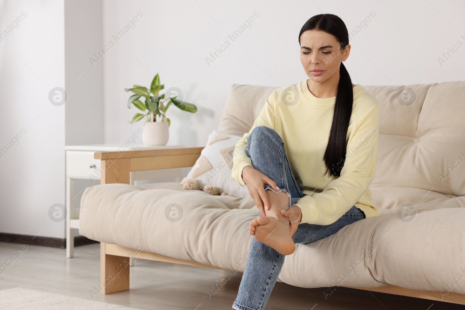 Photo of Woman rubbing sore leg on sofa at home, space for text