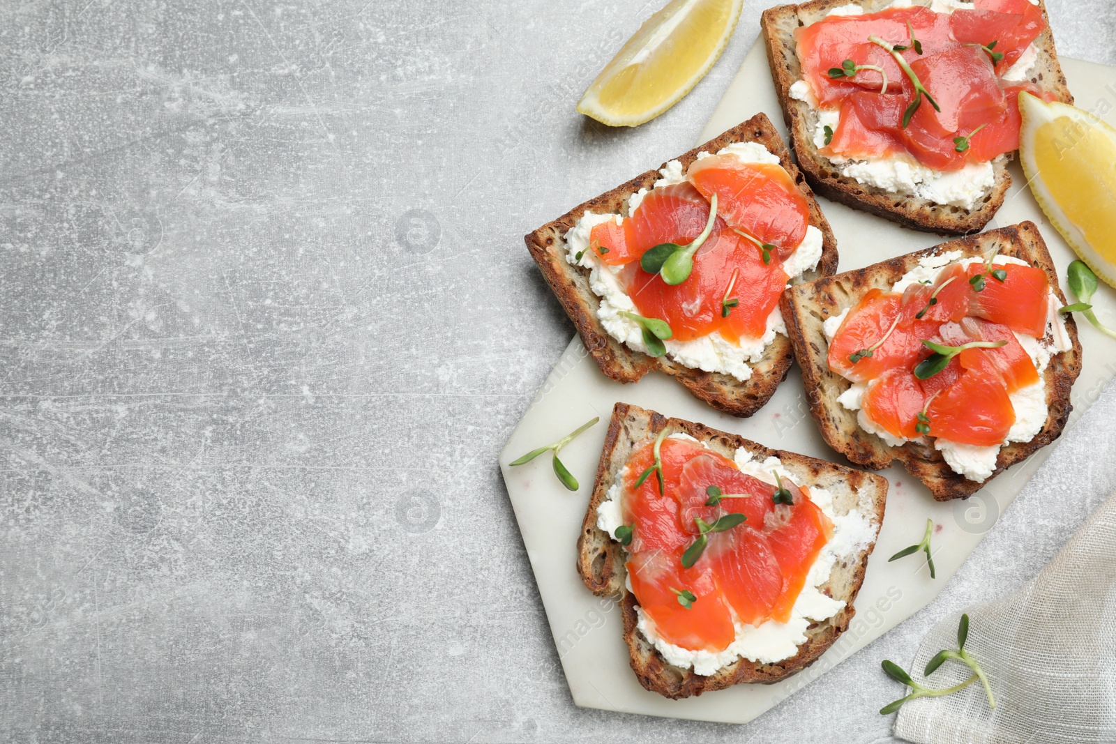 Photo of Delicious sandwiches with cream cheese, salmon and microgreens on light grey table, flat lay. Space for text