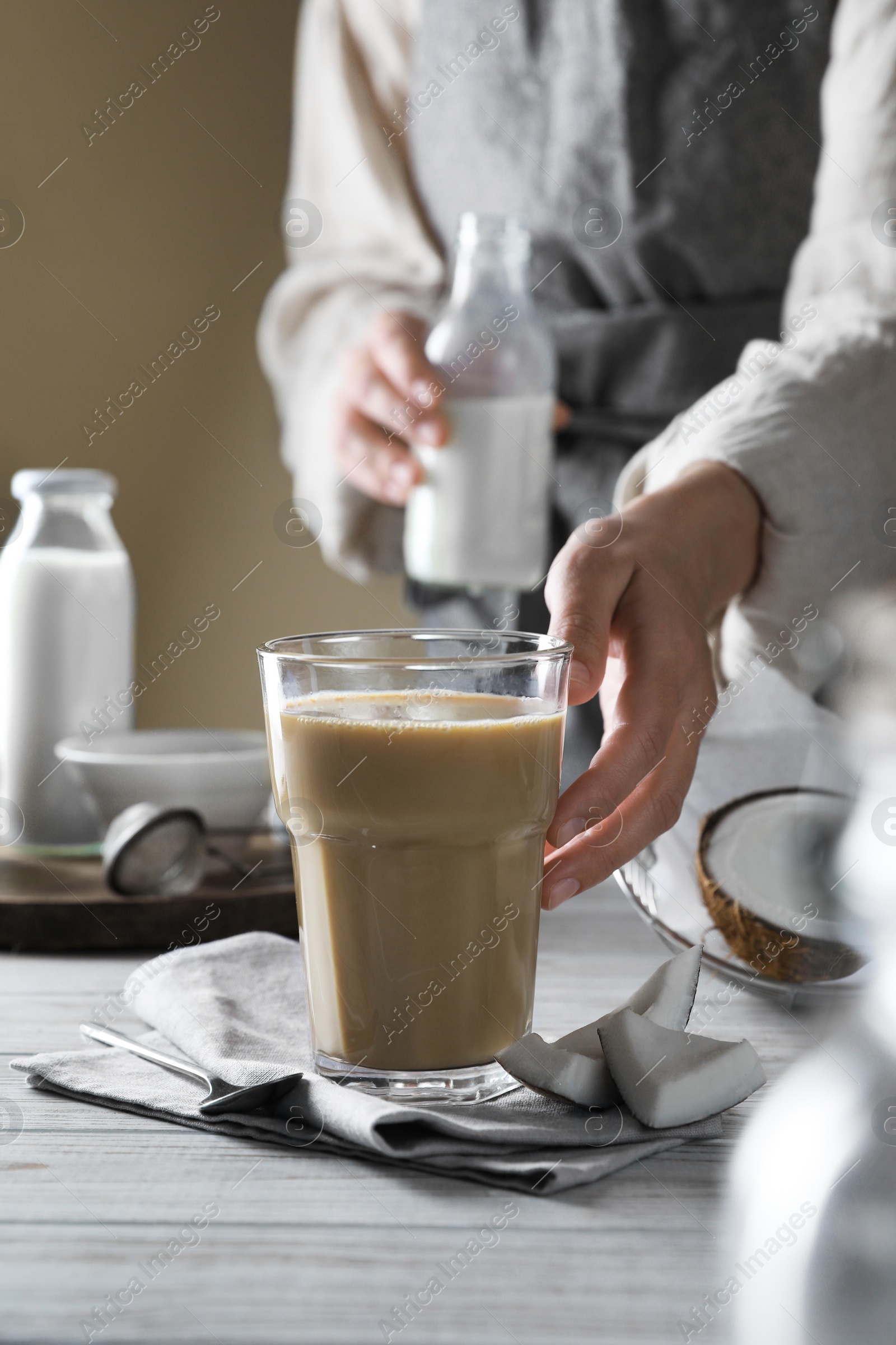 Photo of Woman with glass of coffee and coconut milk at white wooden table, closeup