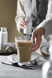 Photo of Woman with glass of coffee and coconut milk at white wooden table, closeup