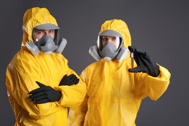 Photo of People in chemical protective suits with blood sample on grey background. Virus research