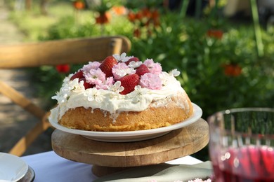 Photo of Delicious homemade cake decorated with fresh strawberries and spring flowers on table in garden