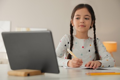 Photo of Little girl doing homework with modern tablet at home