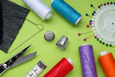 Flat lay composition with thimbles and different sewing tools on green background