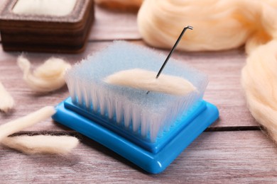 Photo of Felting wool, brush and needle on wooden table, closeup