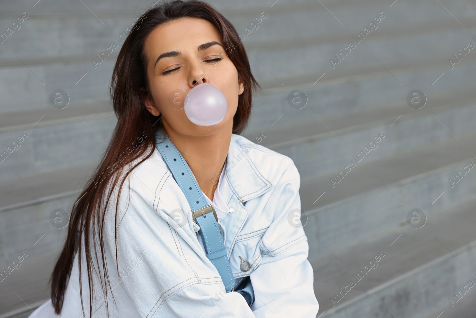 Photo of Stylish woman blowing gum near stairs outdoors, space for text