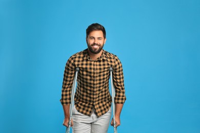 Photo of Young man with axillary crutches on light blue background