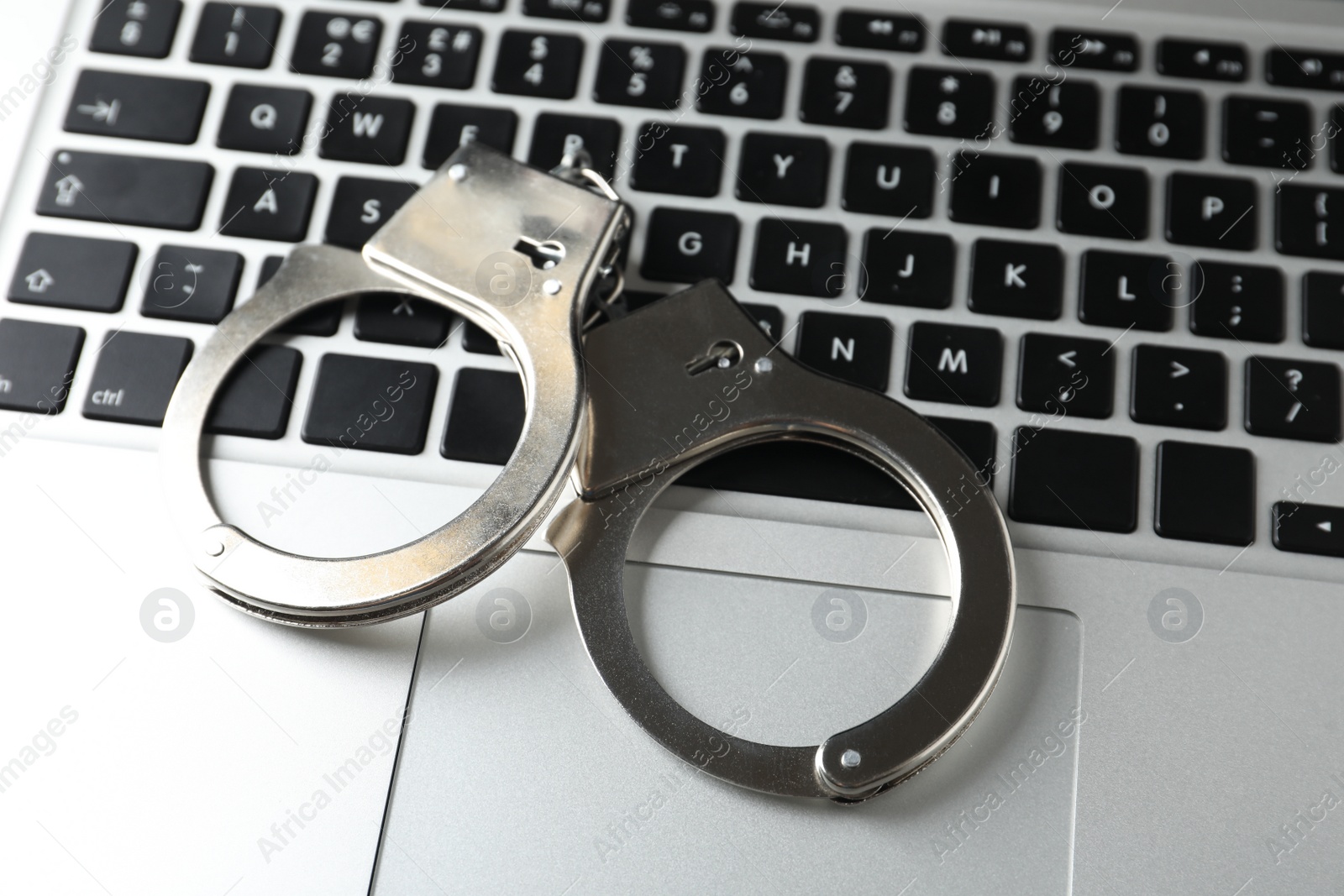 Photo of Handcuffs on modern laptop, closeup. Cyber crime