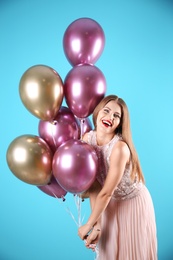 Young woman with air balloons on color background