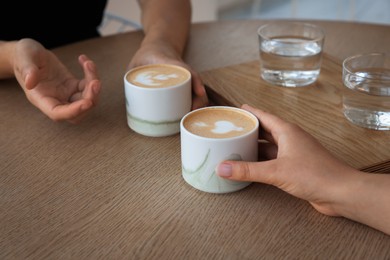 Friends drinking coffee at wooden table in cafe, closeup