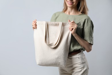 Happy young woman with blank eco friendly bag on light background, closeup