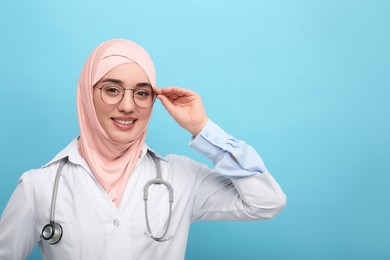 Muslim woman wearing hijab and medical uniform with stethoscope on light blue background, space for text