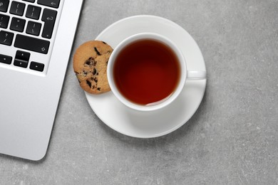 Photo of Chocolate chip cookie, cup of tea and laptop on light grey table, flat lay