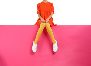 Woman wearing yellow tights and stylish shoes sitting on color background, closeup