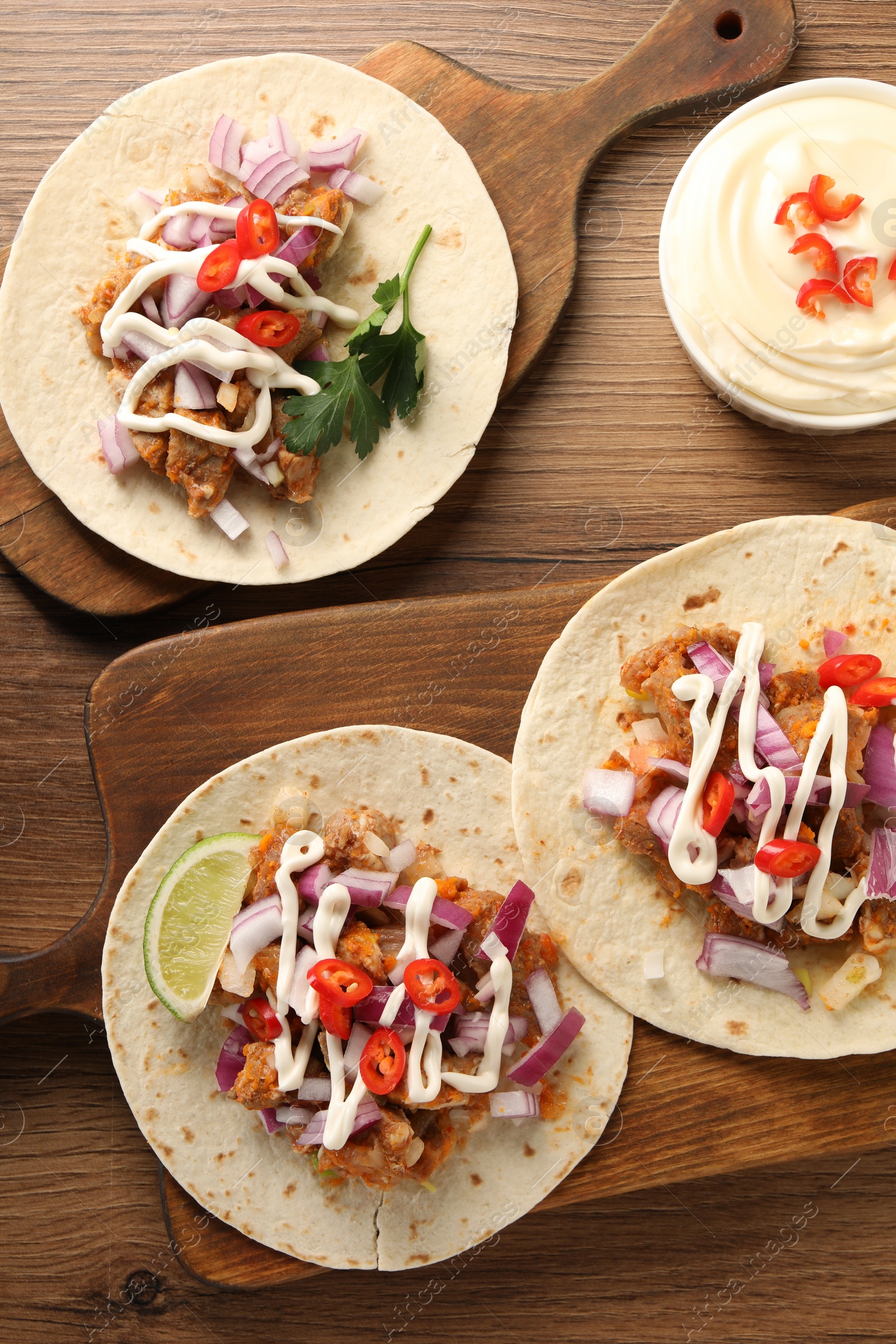 Photo of Delicious tacos with vegetables, meat and sauce on wooden table, flat lay