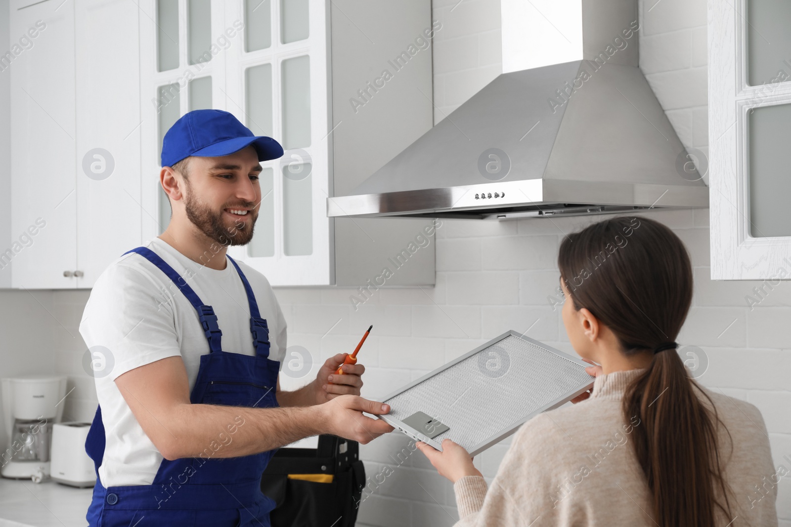 Photo of Woman giving filter of cooker hood to repairman in kitchen