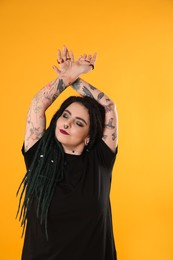Photo of Beautiful young woman with tattoos on arms, nose piercing and dreadlocks against yellow background