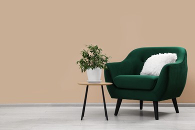 Photo of Stylish armchair and side table with plant near beige wall indoors, space for text
