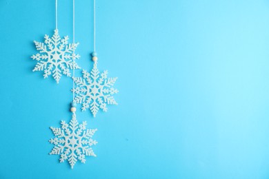 Photo of Beautiful decorative snowflakes hanging on light blue background, space for text