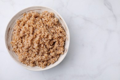 Photo of Tasty wheat porridge in bowl on white marble table, top view. Space for text