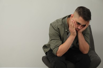 Photo of Sad man sitting near light grey wall. Space for text