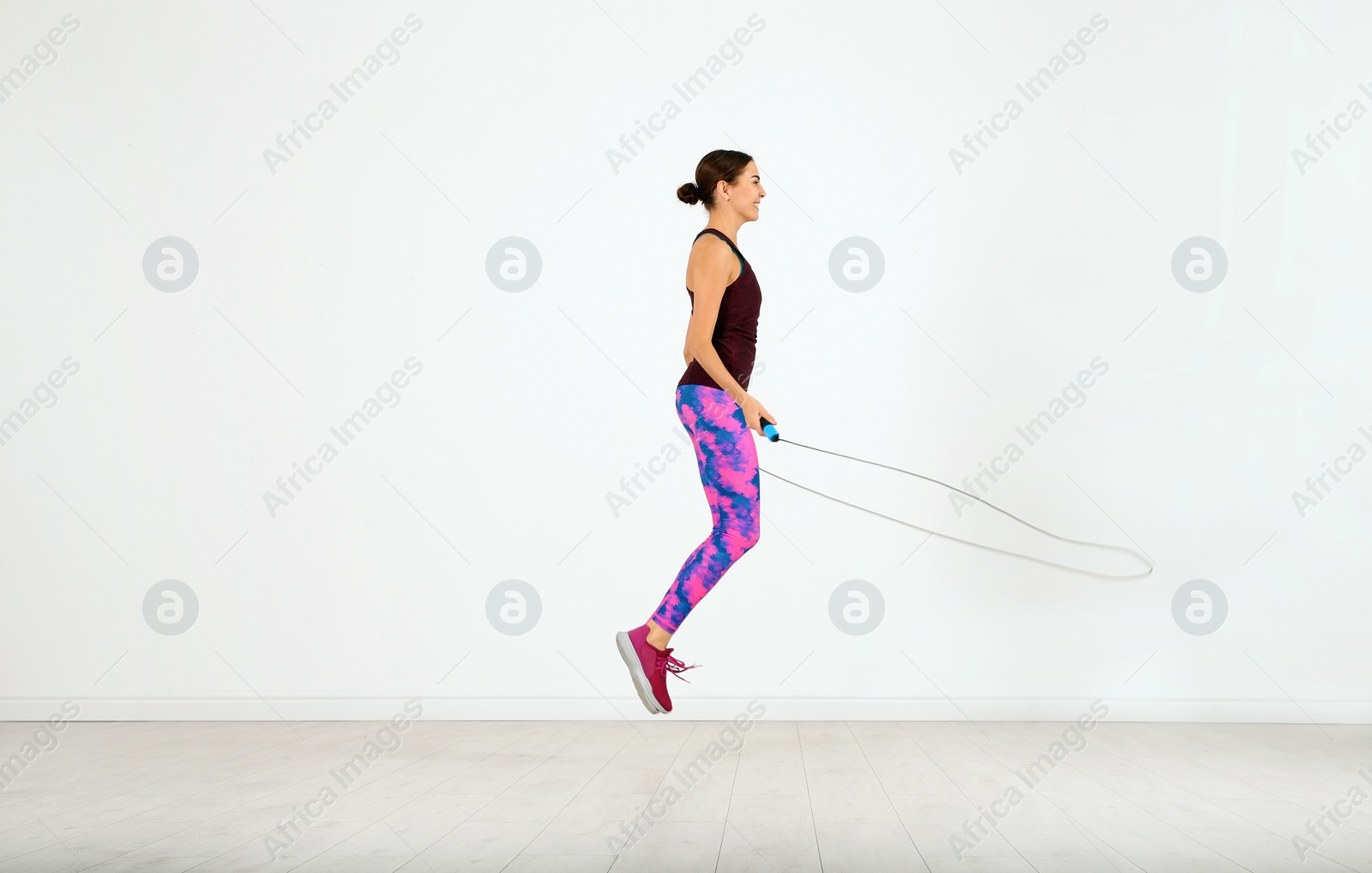 Photo of Young sportive woman training with jump rope in light room