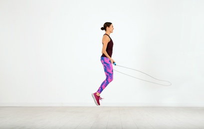 Photo of Young sportive woman training with jump rope in light room