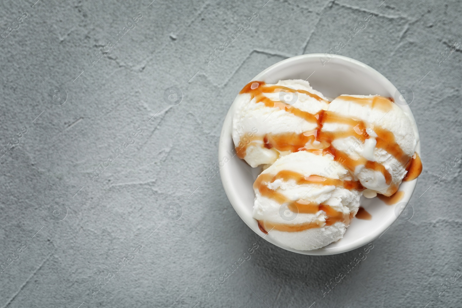 Photo of Tasty ice cream with caramel sauce in bowl on table