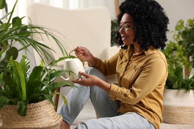 Happy woman watering beautiful houseplants at home