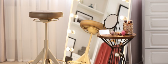 Makeup room. Stylish mirror with light bulbs, beauty products on side table and chair indoors, banner design