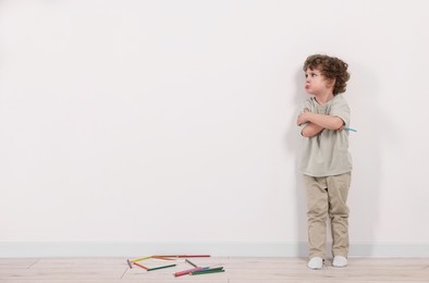 Photo of Upset little boy with pencil near white wall indoors. Space for text
