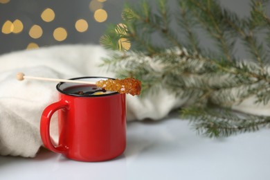 Photo of Stick with sugar crystals and cup of drink on white table against blurred festive lights, space for text