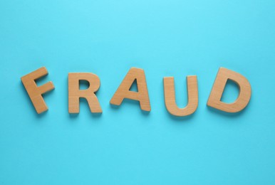 Word Fraud made of wooden letters on light blue background, flat lay