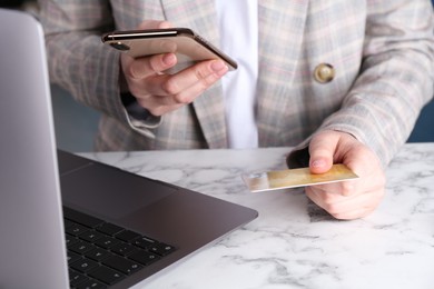 Photo of Online payment. Woman with laptop, smartphone and credit card at white marble table, closeup