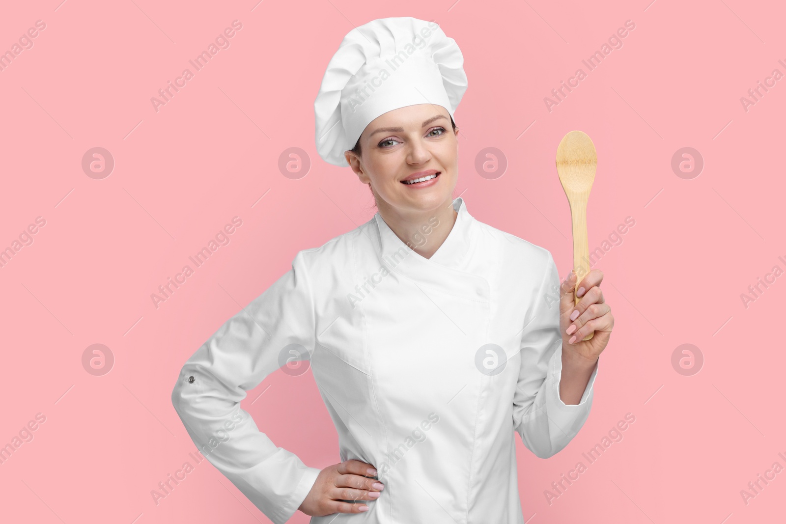 Photo of Happy chef in uniform holding wooden spoon on pink background