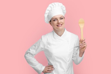 Photo of Happy chef in uniform holding wooden spoon on pink background