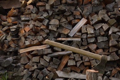 Photo of Ax with wooden handle near log pile