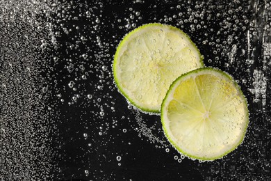 Photo of Juicy lime slices in soda water against black background, closeup. Space for text