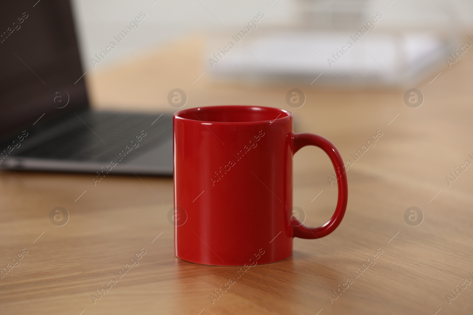 Photo of Red ceramic mug and laptop on wooden table at workplace