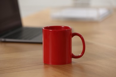 Photo of Red ceramic mug and laptop on wooden table at workplace