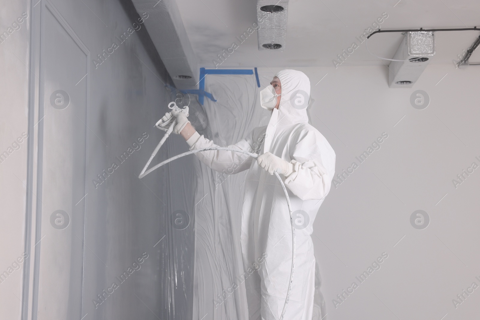 Photo of Decorator dyeing wall in grey color with spray paint indoors